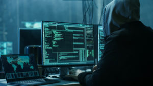 Dangerous Hooded Hacker Breaks into Government Data Servers and Infects Their System with a Virus. His Hideout Place has Dark Atmosphere, Multiple Displays, Cables Everywhere.