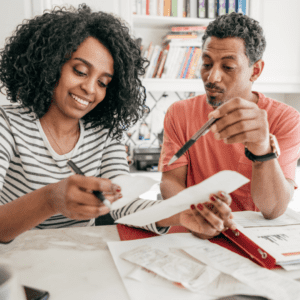 A smiling woman and man sit at a table reviewing documents together.