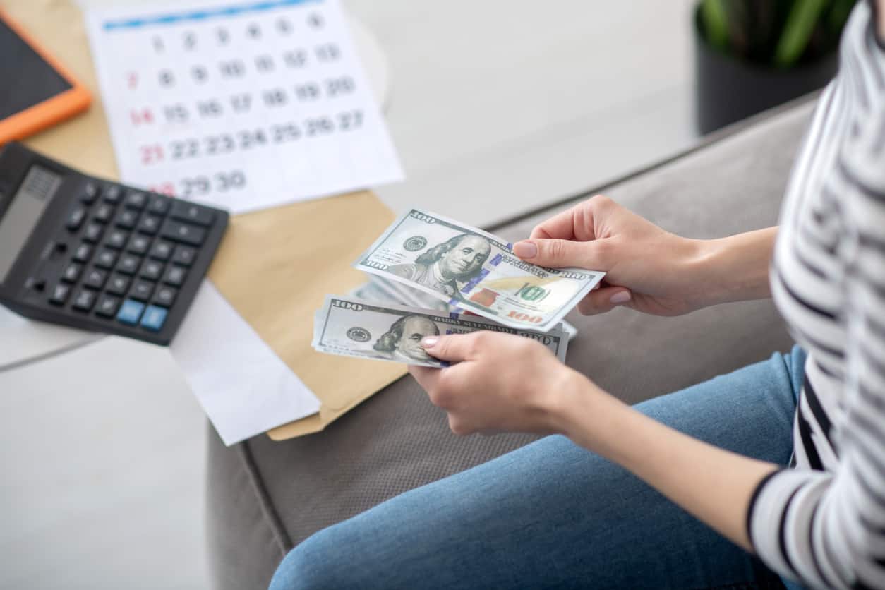 Woman counting dollar bills at home for her monthly budget - setting personal finance resolutions.