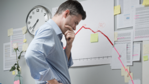 A man in a blue shirt stands thoughtfully in front of a wall.