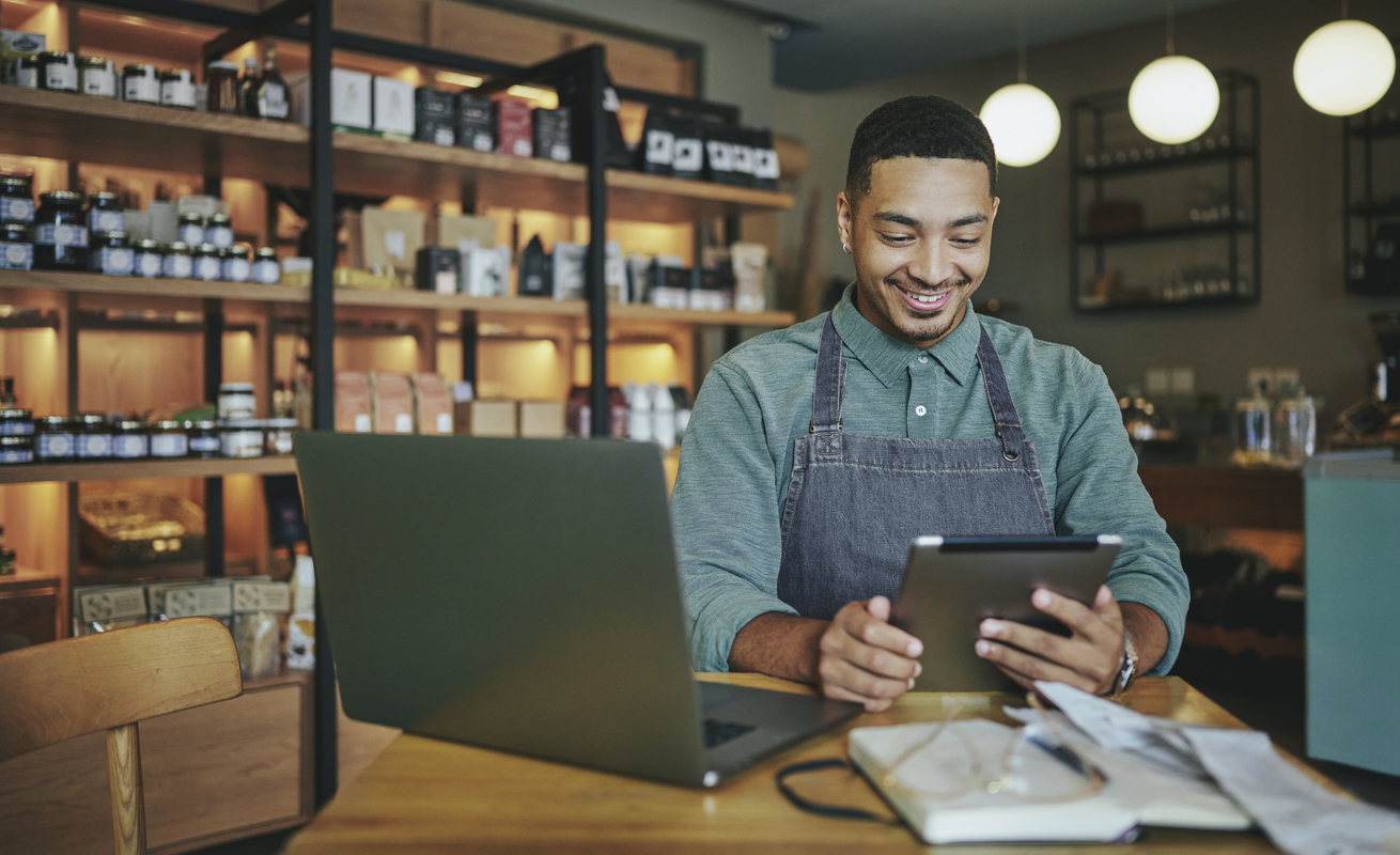 Male small business owner working on a tablet and laptop in his shop - small business growth process.