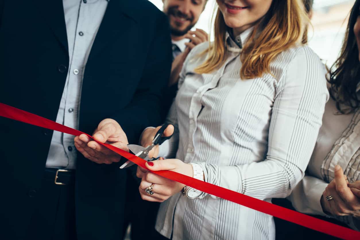 Businesswoman and her colleagues cutting a red ribbon during their business opening - business owners in 2023.
